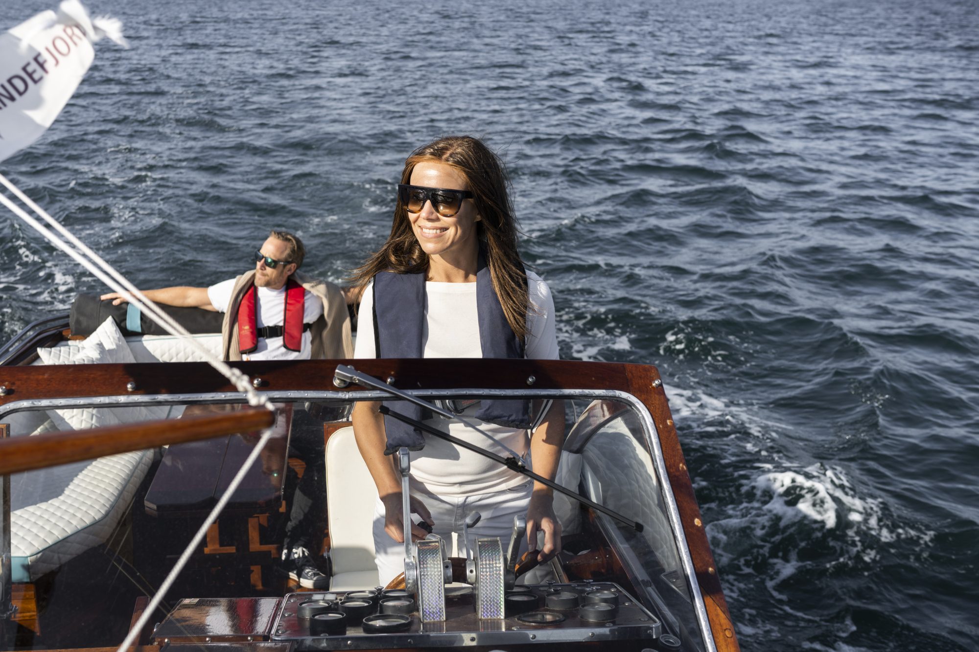 Dame styrer båt med mann i bakgrunnen. Jotun Yachting.